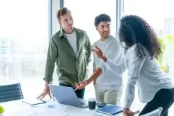 "Equipo de trabajo analizando información frente a un portátil en una oficina luminosa"